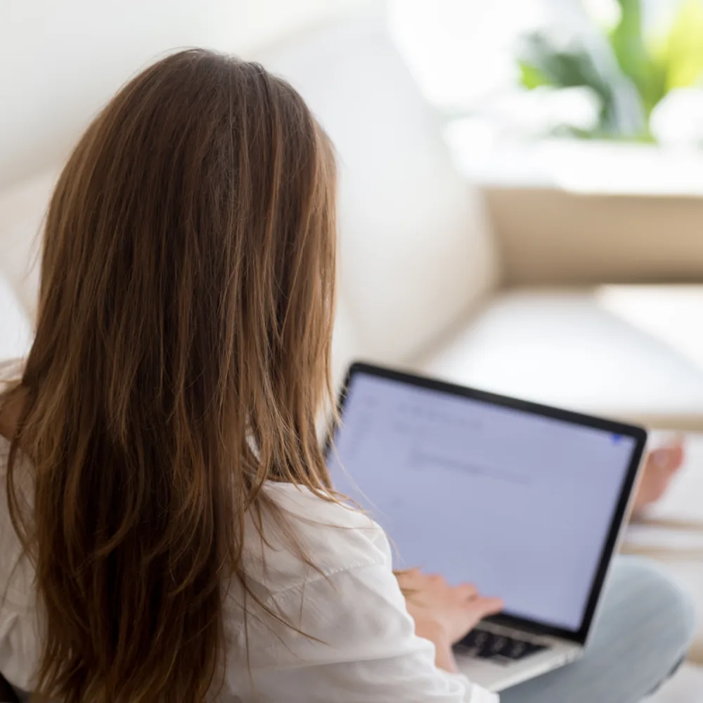 Woman sitting on a sofa using a laptop, representing job seekers reporting spam or suspicious contact attempts online.